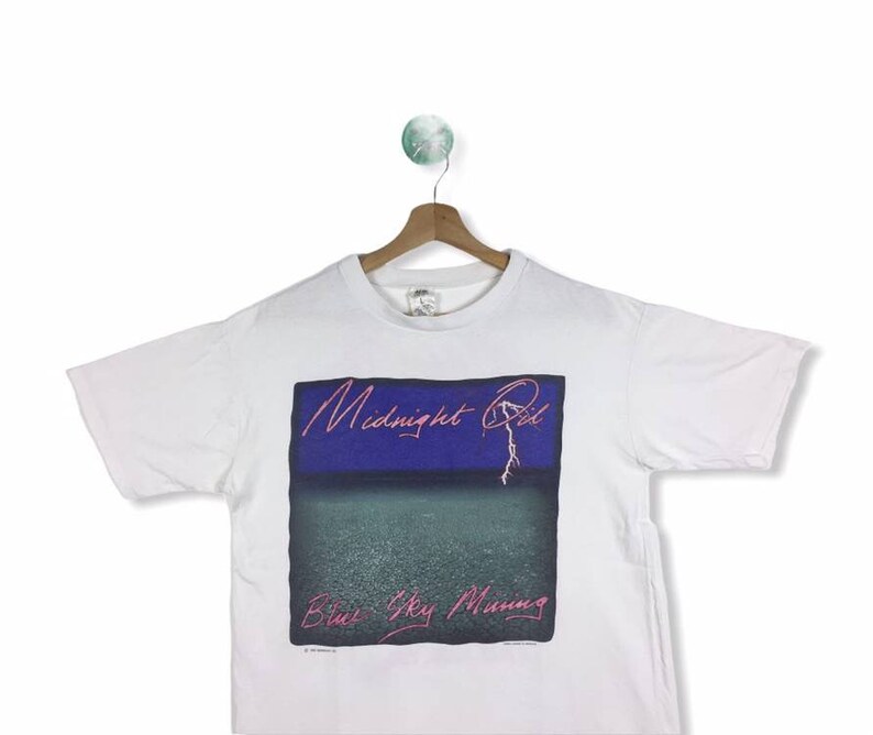 May include: White t-shirt with a graphic print of the album cover for "Midnight Oil - Blue Sky Mining".