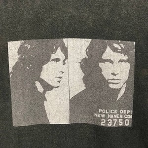 Puede incluir: Camiseta negra con una imagen en blanco y negro de la cara de un hombre. La imagen es una foto de estilo mugshot con el texto "POLICE DEPT NEW HAVEN CON 23750" debajo de la imagen.