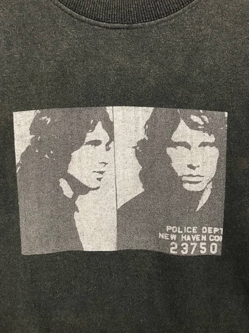 Puede incluir: Camiseta negra con una imagen en blanco y negro de la cara de un hombre. La imagen es una foto de estilo mugshot con el texto "POLICE DEPT NEW HAVEN CON 23750" debajo de la imagen.