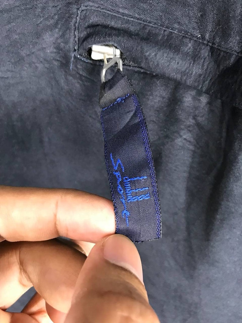 May include: A black zipper pull with a blue embroidered label that reads "Sport III".