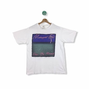May include: White t-shirt with a graphic of the band Midnight Oil's album cover for "Blue Sky Mining". The album cover features a blue and purple sky with a lightning bolt and the text "Midnight Oil" in pink.