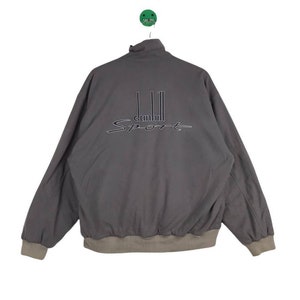 May include: A gray, zip-up jacket with a brown ribbed collar and cuffs. The jacket has the text "dunhill Sport" embroidered on the back.