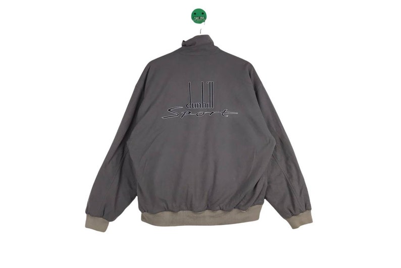 May include: A gray, zip-up jacket with a brown ribbed collar and cuffs. The jacket has the text "dunhill Sport" embroidered on the back.