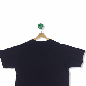 K&ouml;nnte beinhalten: Ein schwarzes T-Shirt mit kurzen &Auml;rmeln, das an einem Holzb&uuml;gel h&auml;ngt. Das T-Shirt ist einfarbig und hat keine sichtbaren Grafiken oder Texte.