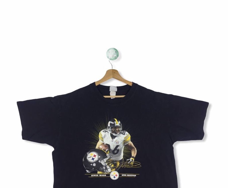 K&ouml;nnte beinhalten: Schwarzes T-Shirt mit einem Grafikdruck von Hines Ward, einem Wide Receiver der Pittsburgh Steelers, der eine schwarz-gelbe Uniform tr&auml;gt und einen Football h&auml;lt. Der Text "Hines Ward" und "Wide Receiver" ist unter dem Grafikdruck aufgedruckt.