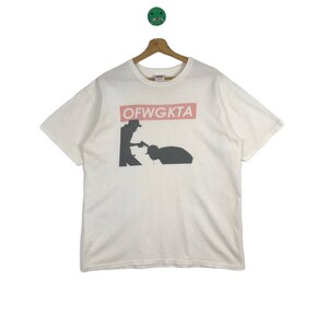 May include: White t-shirt with a black and white graphic of two figures. The text "OFWGKTA" is printed in a red rectangle.