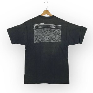 Puede incluir: Camiseta negra con una impresi&oacute;n blanca en la espalda que dice "INCIDENT REPORT" e incluye un bloque de texto. El texto incluye las palabras "Asunto: El evento", "Fecha: 8 de junio de 1997" y "Ubicaci&oacute;n: La parte de atr&aacute;s de la pizzer&iacute;a de John".