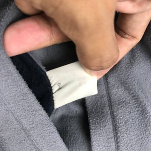 May include: Close-up of a gray hooded sweatshirt with a black lining. The tag on the inside of the hood reads "B-L".