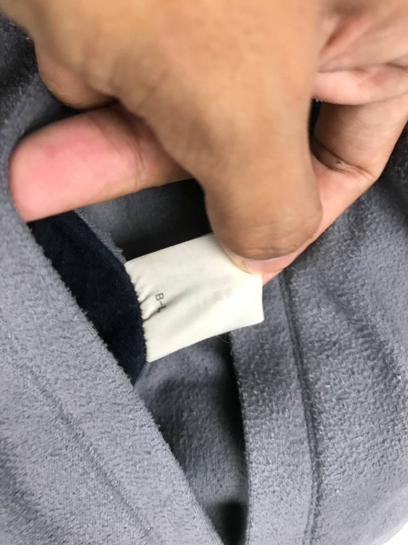 May include: Close-up of a gray hooded sweatshirt with a black lining. The tag on the inside of the hood reads "B-L".