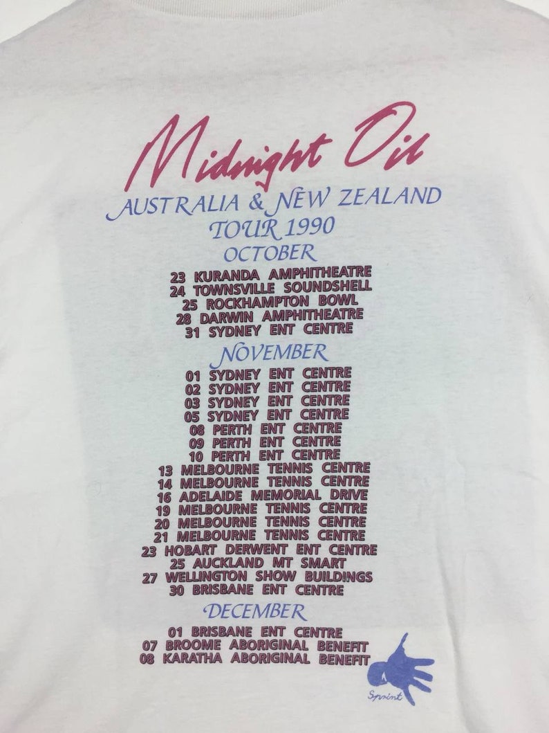 May include: A white t-shirt with a pink and purple print of the Midnight Oil band tour dates for Australia and New Zealand in 1990. The tour dates are listed for October, November, and December.