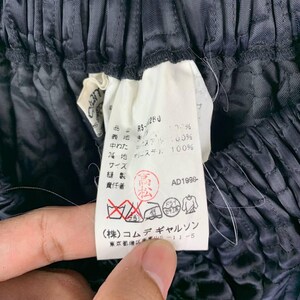 May include: Close-up of black fabric with a tag. The tag has Japanese text and symbols, including "RS-1280" and "AD1998-". The fabric appears to be quilted or textured, with a slightly shiny finish. The image is well-lit, showing the details of the fabric and tag.