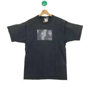 Puede incluir: Camiseta negra con una imagen descolorida de dos hombres, posiblemente m&uacute;sicos, con el texto "Police Dept. New York City 222222" impreso debajo de la imagen.