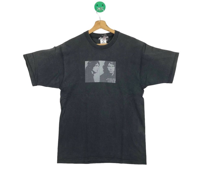 Puede incluir: Camiseta negra con una imagen descolorida de dos hombres, posiblemente m&uacute;sicos, con el texto "Police Dept. New York City 222222" impreso debajo de la imagen.