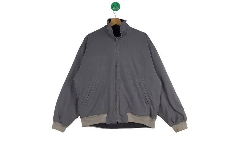 May include: A gray zip-up bomber jacket with a beige lining. The jacket has two pockets on the front and a ribbed collar.