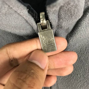 May include: Close-up of a silver zipper pull with the word "Salomon" printed on it.