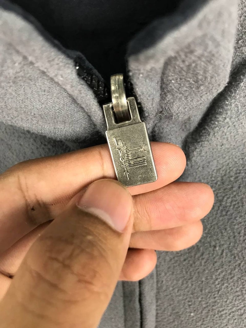 May include: Close-up of a silver zipper pull with the word "Salomon" printed on it.