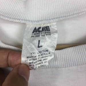 May include: White cotton t-shirt tag with the text "ACME T-SHIRT COMPANY PH (02) 591 5111" and "101% COTTON MADE IN AUSTRALIA DO NOT IRON IF DECORATED WASH MACHINE WARM DO NOT TUMBLE DRY DO NOT BLEACH".
