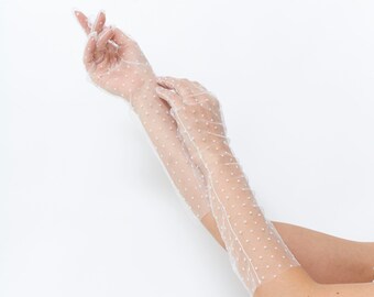 Puede incluir: Un par de guantes largos de encaje blanco con pequeños lunares blancos. Los guantes son largos y llegan más allá de los codos.