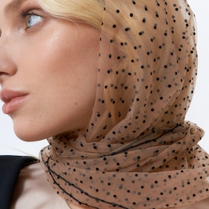 May include: A brown sheer scarf with black polka dots. The scarf is made of a lightweight material and has a delicate, feminine look.
