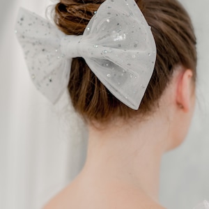 May include: A white tulle bow with silver glitter accents, worn in a woman's hair.