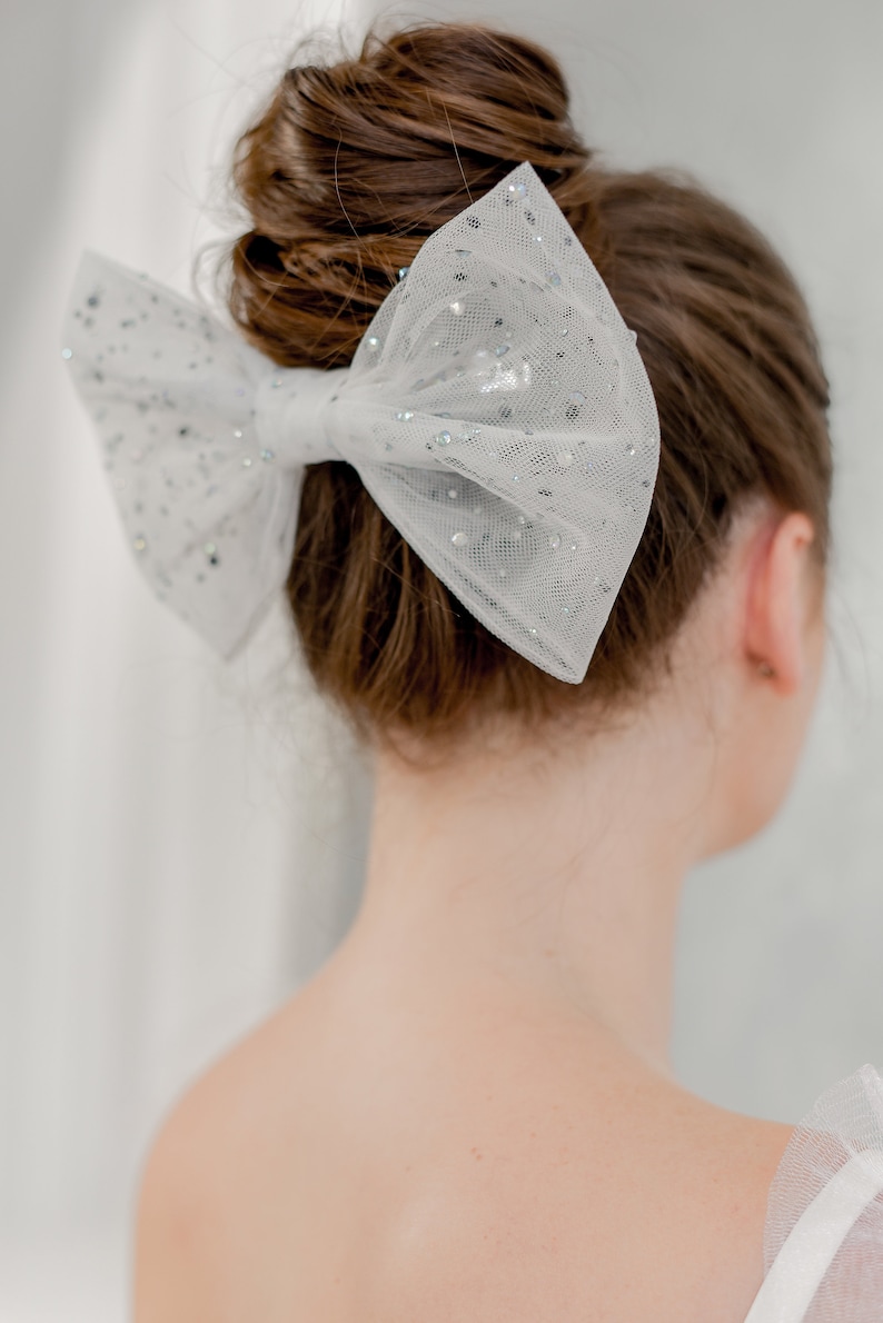 May include: A white tulle bow with silver glitter accents, worn in a woman's hair.