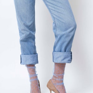 May include: A pair of light blue jeans with the cuffs rolled up, worn with light blue polka dot sheer socks and nude high-heeled pumps.
