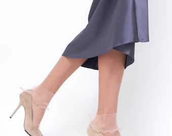 May include: A pair of nude heels with a delicate ruffle detail on the socks. The heels are made of suede and have a pointed toe. The socks are sheer and have a ruffled edge.