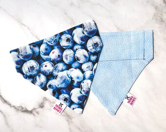 May include: Two dog bandanas, one with a blue and white blueberry print and the other with a light blue and white polka dot print. Both bandanas have the text "Rebel Bones" in pink.