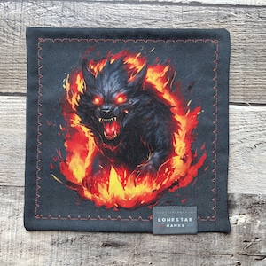 May include: A black square handkerchief with a fiery wolf design. The wolf is surrounded by flames, with glowing red eyes and an open mouth. The handkerchief has a stitched border and a small label that reads "LONESTAR HANKS".