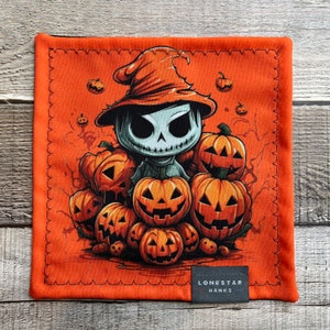 May include: Orange Halloween-themed handkerchief featuring a cartoon character with a skull face wearing a witch hat, surrounded by carved pumpkins. The handkerchief has a stitched border and a small tag that reads "LONESTAR HANKS".