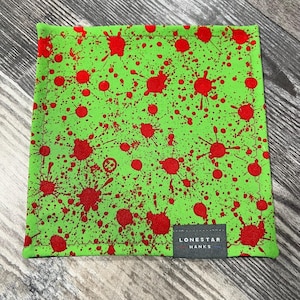 May include: Square green fabric with a red splatter pattern. The fabric has a stitched border and a small rectangular tag that reads "LONESTAR HANKS".