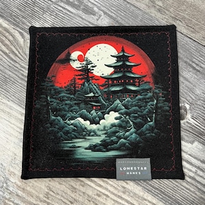 May include: Black square fabric with a Japanese-inspired landscape design. The artwork features a red sun, a white moon, and a pagoda surrounded by trees. The fabric has a red stitched border and a small tag that reads "LONESTAR HANKS."