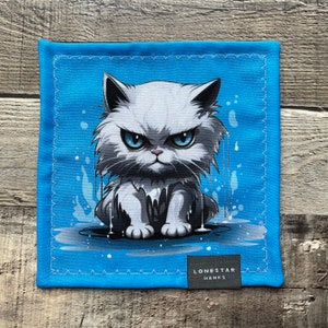 May include: Square blue handkerchief featuring an illustration of an angry white cat with blue eyes. The cat is depicted with water droplets and sitting in a puddle. The handkerchief has a stitched border and a small label that reads "LONESTAR HANKS."