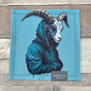May include: A square, light blue handkerchief featuring a stylized illustration of a goat wearing a blue hoodie and headphones. The goat has large horns and red eyes. The bottom right corner has a small tag that reads "LONESTAR HANKS".