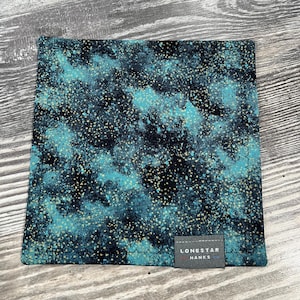 May include: Square, patterned handkerchief with a teal and black speckled design. The fabric has a textured appearance with small gold flecks. A small gray label with the text "LONESTAR HANKS" is sewn on the bottom.