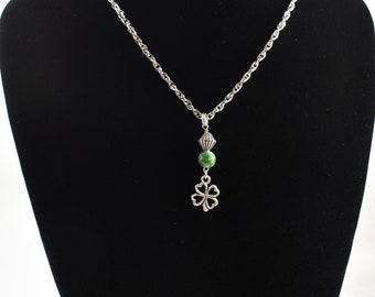 Puede incluir: Un collar de cadena plateada con una cuenta de piedra verde y un dije de trébol de cuatro hojas.