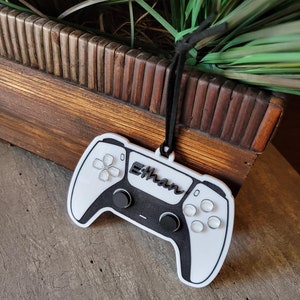 May include: White plastic video game controller ornament with black buttons and the name "Ethan" printed on it.