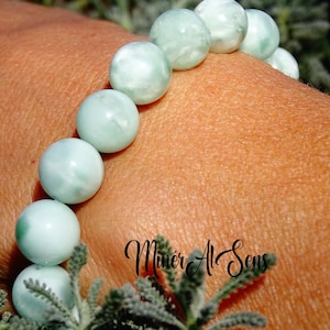 Peut inclure: Un bracelet composé de perles de pierres précieuses vert clair et blanches. Le bracelet est porté au poignet.
