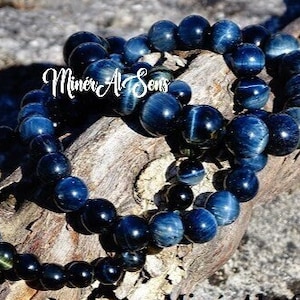 Könnte beinhalten: Drei blaue und schwarze Perlenarmbänder aus Tigerauge. Die Armbänder sind übereinander gestapelt und liegen auf einem Stück Holz.