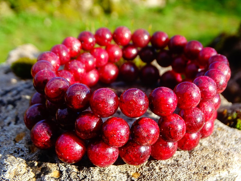 May include: A red gemstone bracelet with multiple strands of round beads. The beads are a deep red color and have a glossy finish.