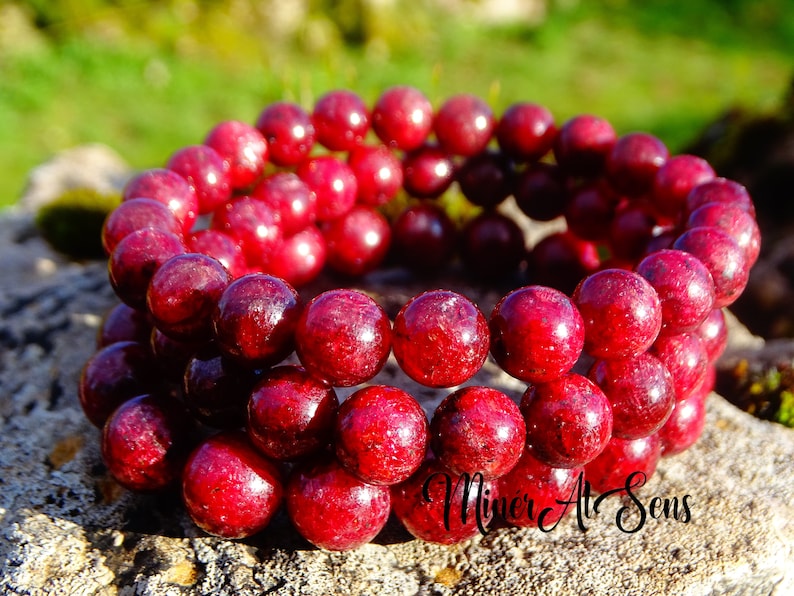 May include: A red gemstone bracelet with round beads. The bracelet is made of multiple strands of beads and is stacked on top of each other.