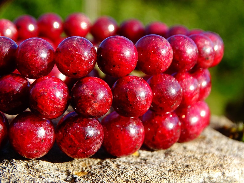 May include: A close-up of a red gemstone bracelet with round beads. The bracelet is made of natural stones and has a polished finish.