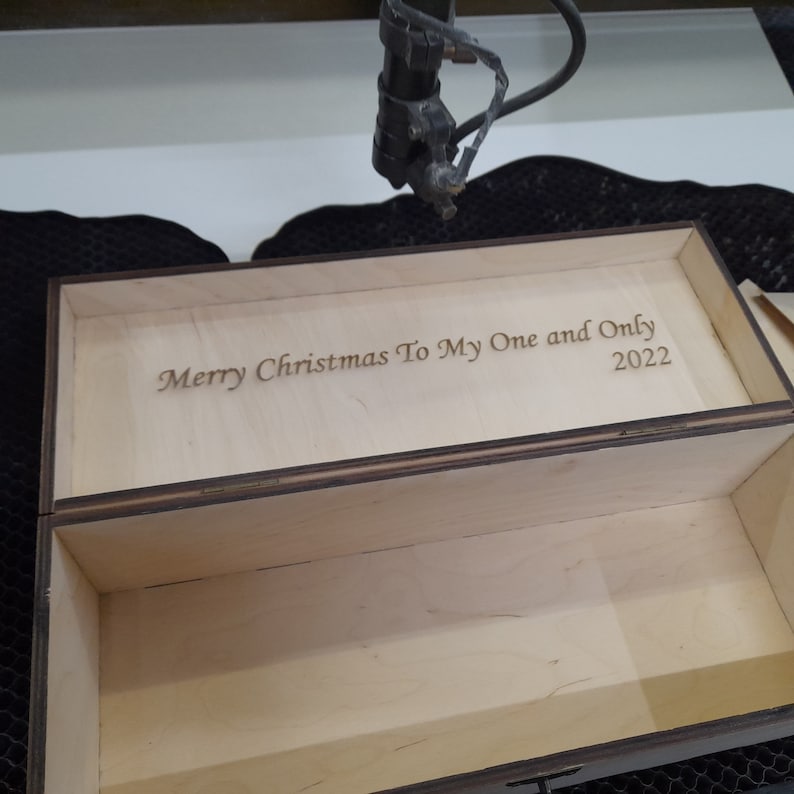 May include: A wooden box with a hinged lid. The lid is open and the inside of the box is visible. The lid is engraved with the text "Merry Christmas To My One and Only 2022".