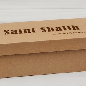 Puede incluir: Caja rectangular de cart&oacute;n marr&oacute;n claro con tapa. En la parte superior, en color marr&oacute;n oscuro, se lee "Saint Shalih". Debajo del texto est&aacute; escrito "Associated with Pellagio LLC".