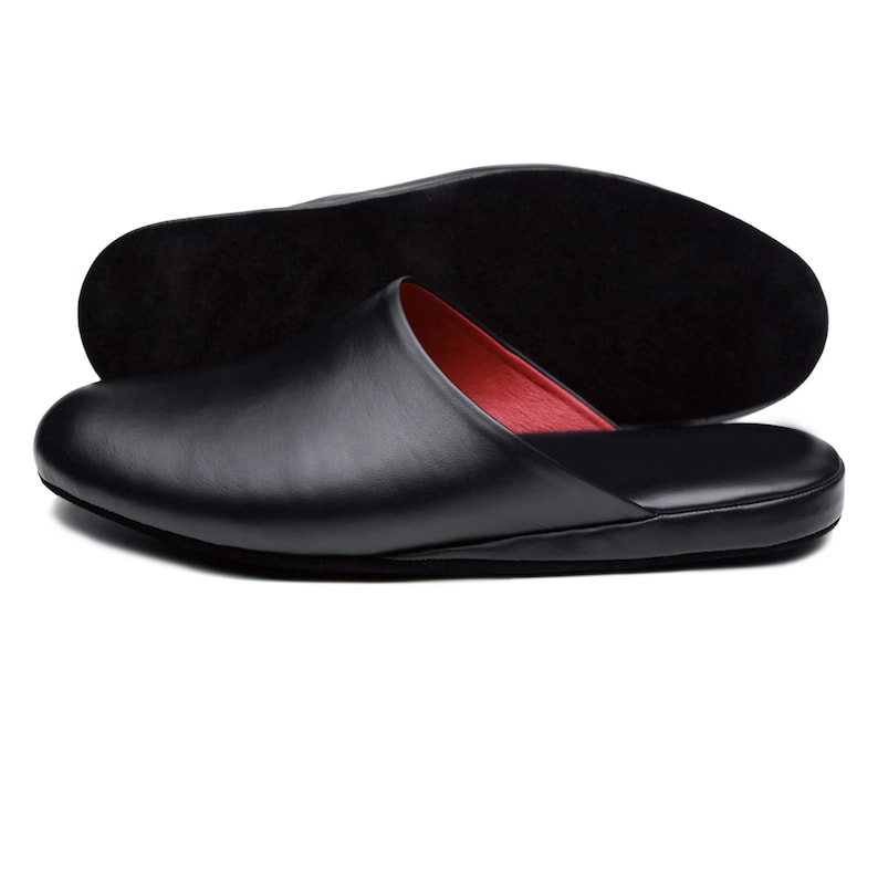 Puede incluir: Zapatilla de cuero negro con interior rojo. La zapatilla se muestra con la suela en el fondo. La zapatilla tiene una punta redondeada y un perfil bajo.
