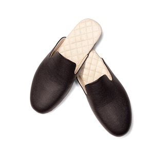 May include: A pair of brown leather slippers with a quilted cream lining. The slippers have a rounded toe and a slip-on design.