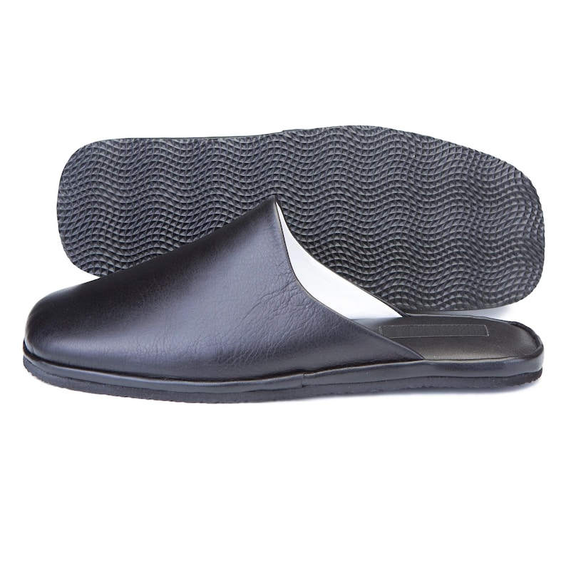 May include: Black leather slippers with a textured rubber sole. The slippers have a white lining and a closed toe.