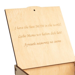 May include: Wooden box with a hinged lid. The lid is open and the inside of the box is visible. The lid has an inscription that reads "I have the best MOM in the world! Liebe Mama wir haben dich lieb! Лучшей мамочке на свете"
