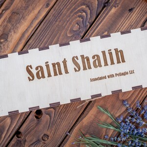 May include: A wooden box with a rope handle. The box is labeled "Saint Shalish" and "Associated with Pellaglo LLC".