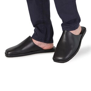 May include: Black leather slippers with a closed toe and a slip-on design. The slippers have a flat sole and a slightly rounded toe.